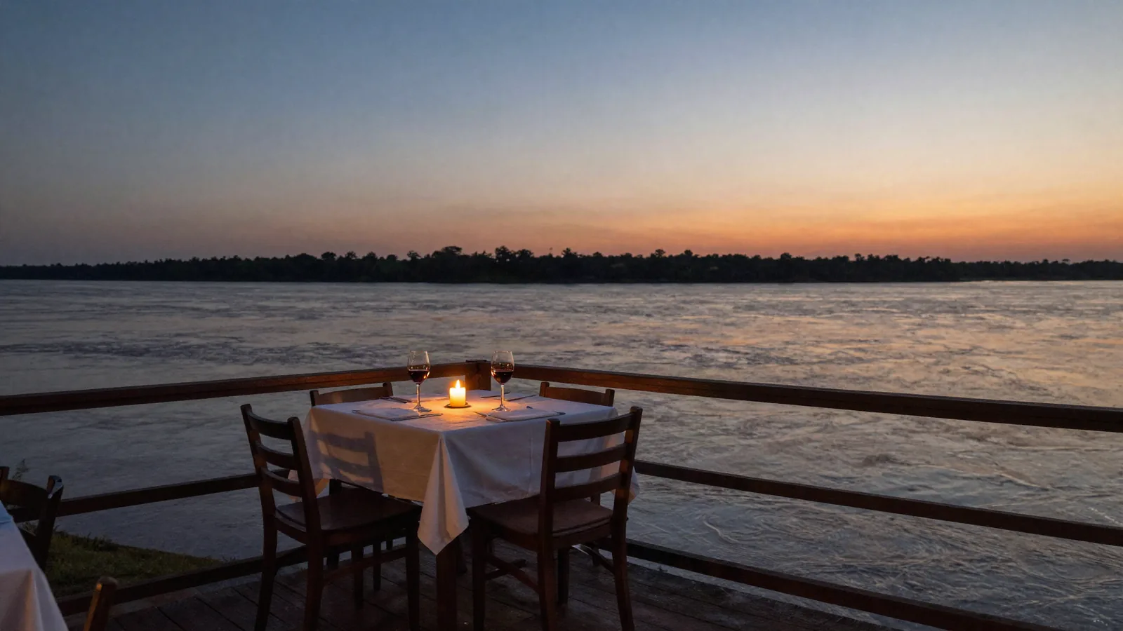 Una mesa puesta en el muelle, sobre el río, al atardecer.