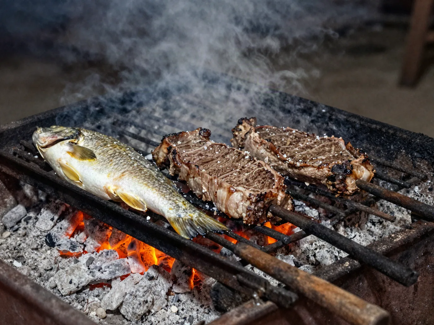 La parrilla de la casa: un pescado de río abierto junto a dos cortes de carne sobre la brasa.